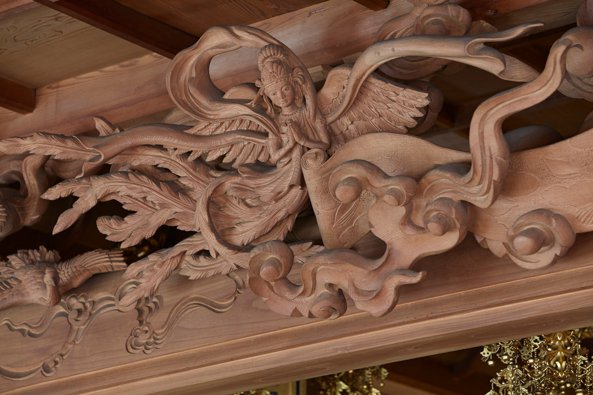 Carved figures and cloud forms in unpainted wood, set within timber architecture